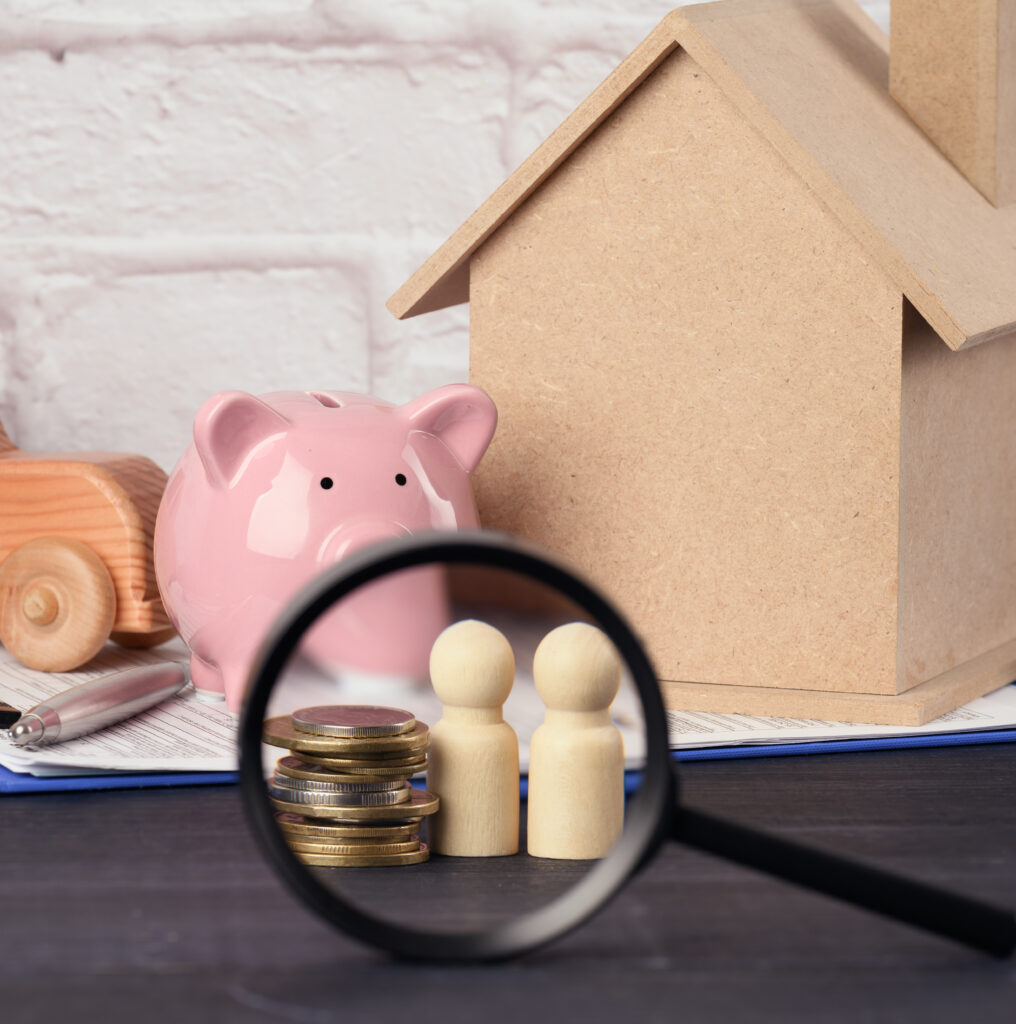 wooden family figurines and pink ceramic piggy bank on blue background. Concept of accumulating cash for buying a house and a car, money in the bank at interest, payment of subsidies